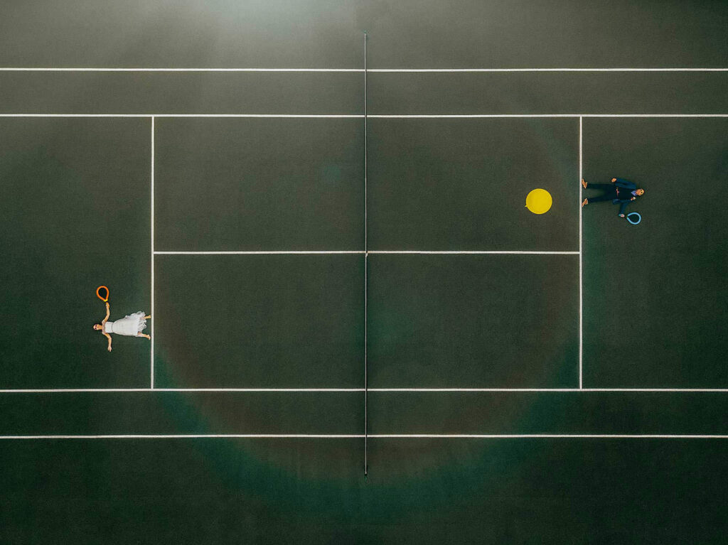 bride and groom lie down on a tennis court